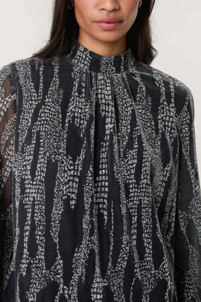 A person dressed in a high-neck blouse featuring a white abstract pattern; the photograph is cropped just below the nose and at the upper arms.