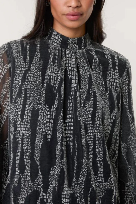 A person dressed in a high-neck blouse featuring a white abstract pattern; the photograph is cropped just below the nose and at the upper arms.