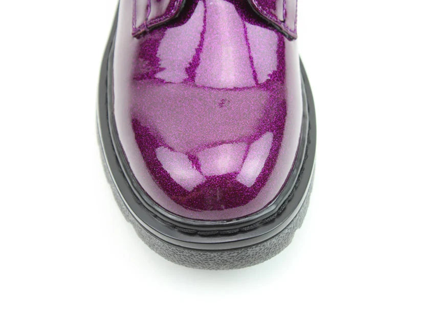 Close-up of the shiny purple toe of a vegan-friendly shoe with black rubber sole, photographed against a white background.