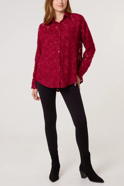 A woman is wearing a long-sleeved, button-up red blouse with knitted detailing and black leggings, paired with black ankle boots, standing against a plain background.