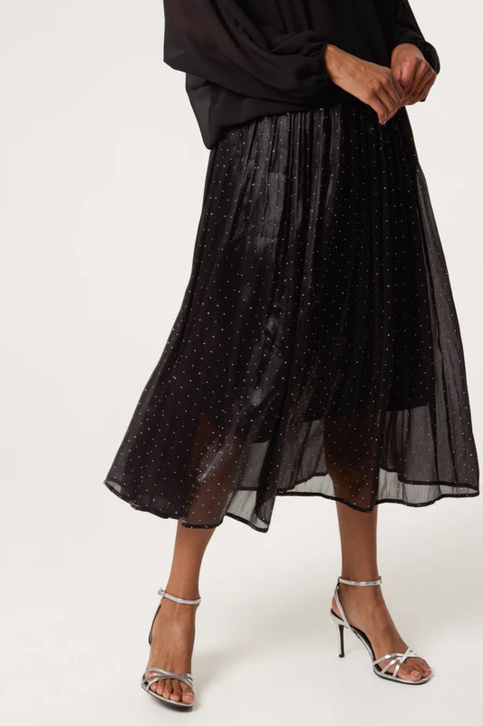 Person wearing a black shimmer midi skirt with small white spots, a black long-sleeved blouse, and silver high-heeled sandals—ideal for elevating any evening skirt outfit.