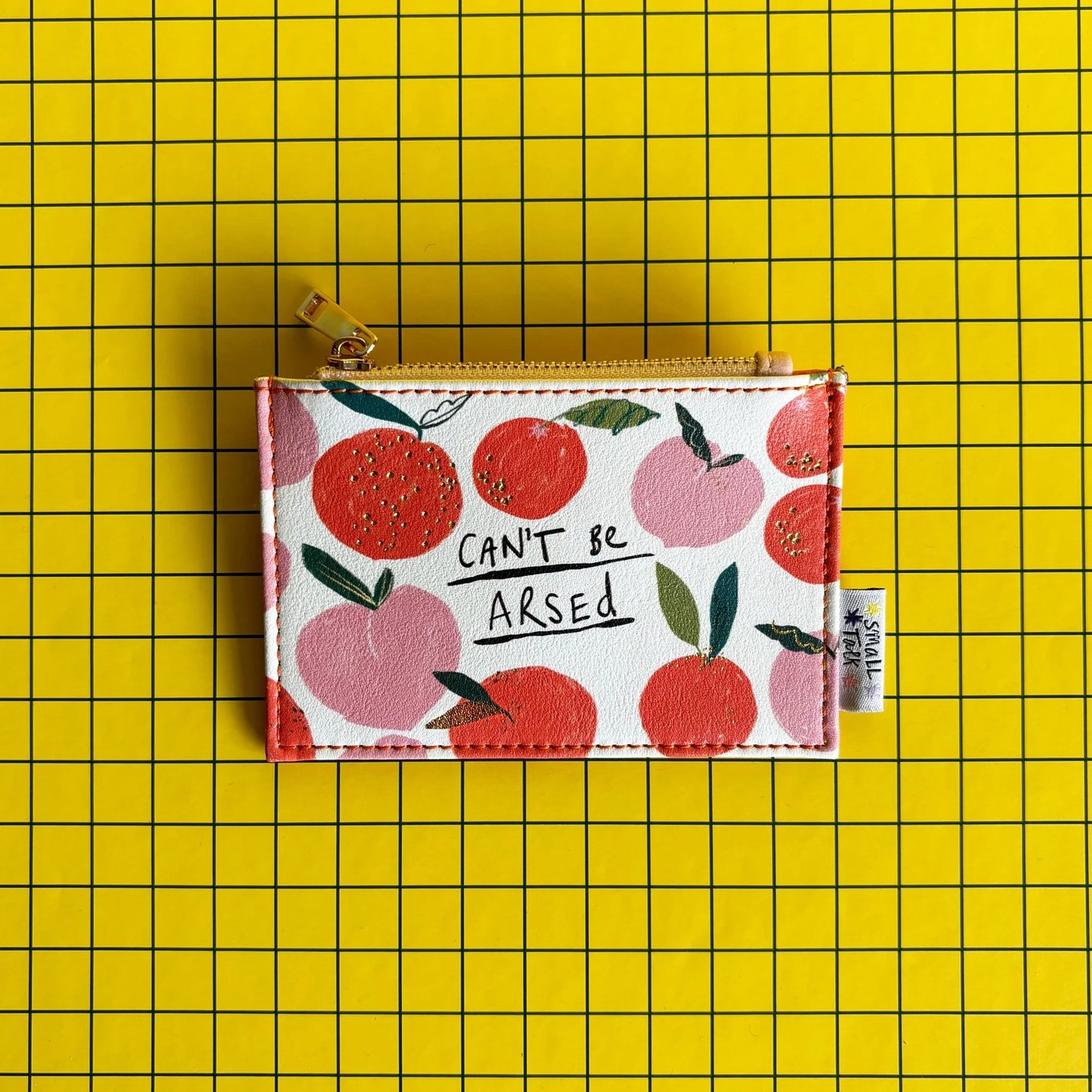 A cheeky purse adorned with a peach motif and the phrase "CANT BE ARSED", this zip purse is a brilliant gift for anyone with a sense of humour. Displayed against a yellow, grid-patterned backdrop.