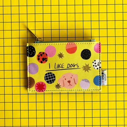 A yellow zip coin purse adorned with colourful dots, a dog illustration, and the words I LIKE DOGS on a yellow grid background—ideal as a present for dog lovers.