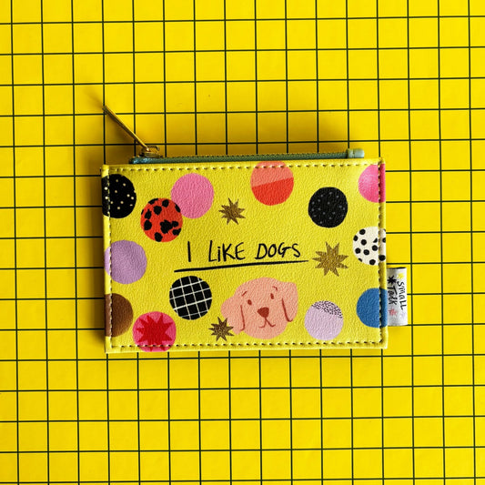 A yellow zip coin purse adorned with colourful dots, a dog illustration, and the words I LIKE DOGS on a yellow grid background—ideal as a present for dog lovers.