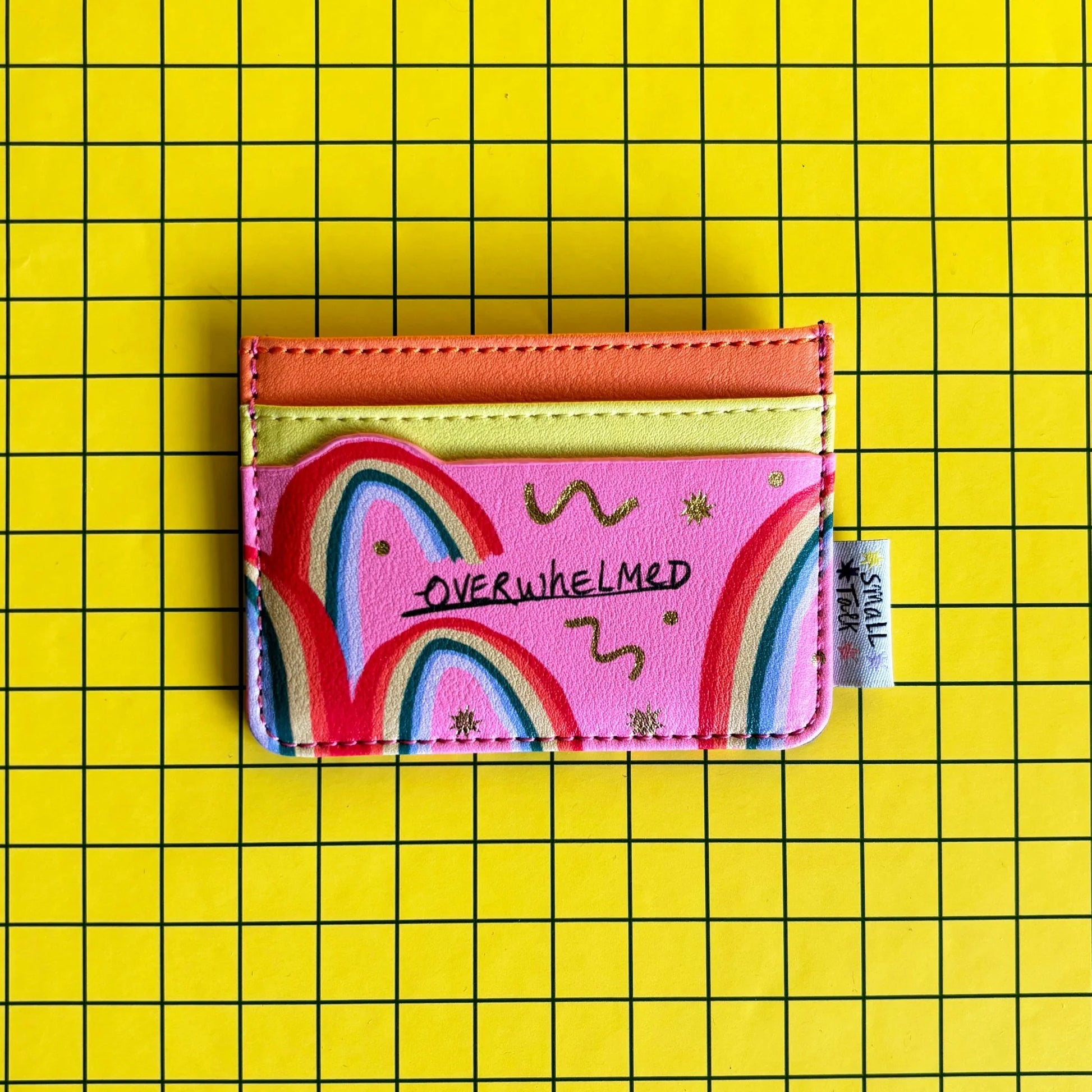 A pink, pocket-sized card holder featuring colourful rainbow designs and the word OVERWHELMED, set against a yellow grid background—ideal as a quirky gift for mates.