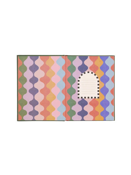 An open hardback notebook shows vibrant patterns on its pages, featuring a blank arched label bordered by black squares on the right—ideal for stationery enthusiasts.