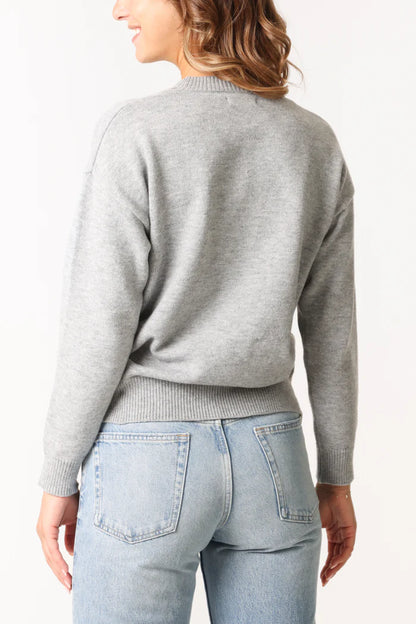 A person in a cosy grey jumper and light blue jeans is seen from behind against a plain background.