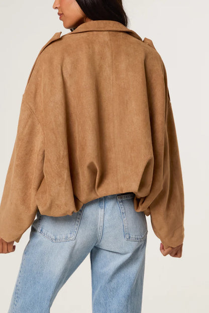 A person is wearing a tan, vegan-friendly jacket with an oversized fit and light blue jeans, photographed from behind against a plain background.