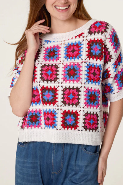 A person wearing a boxy crochet top featuring a colourful granny square pattern in red, pink, blue, and white, teamed with blue denim trousers.