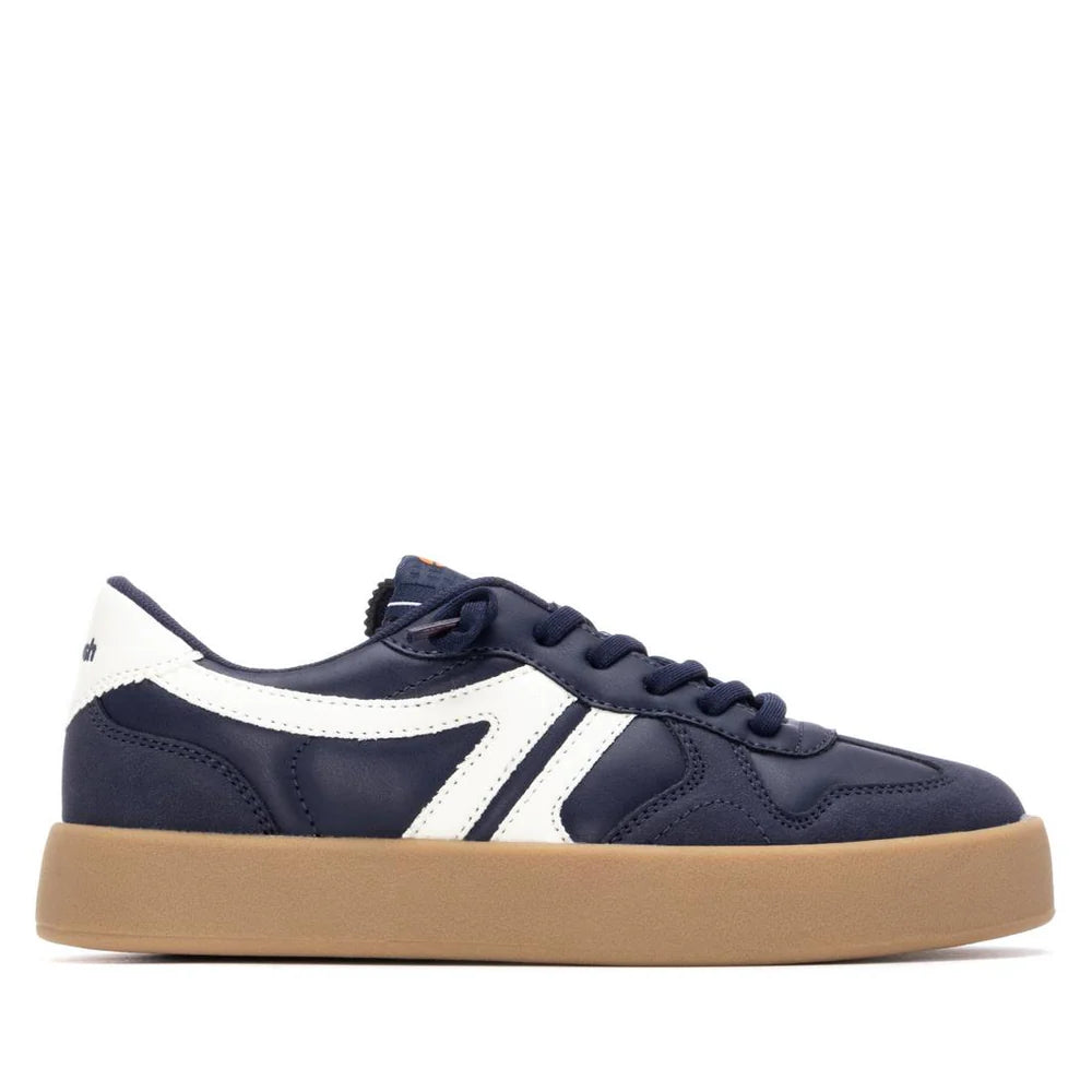A navy blue vegan trainer with white detailing and a white logo, featuring a gum-coloured non-slip sole and navy laces, viewed from the side. PETA-certified for cruelty-free style.