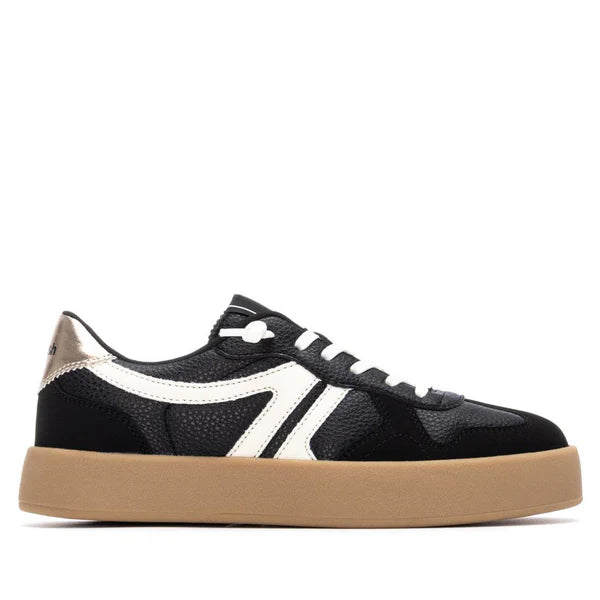 A black vegan trainer with white accents, white laces, a tan gum sole, and a metallic heel detail, shown in side profile—stylish PETA-certified footwear for everyday wear.