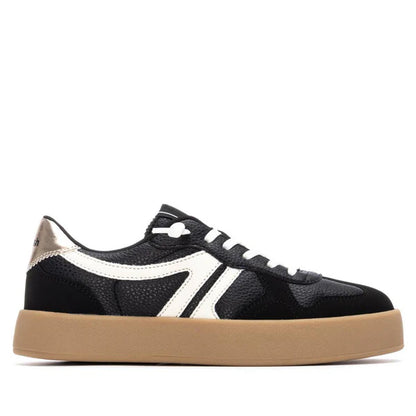 A black vegan trainer with white accents, white laces, a tan gum sole, and a metallic heel detail, shown in side profile—stylish PETA-certified footwear for everyday wear.